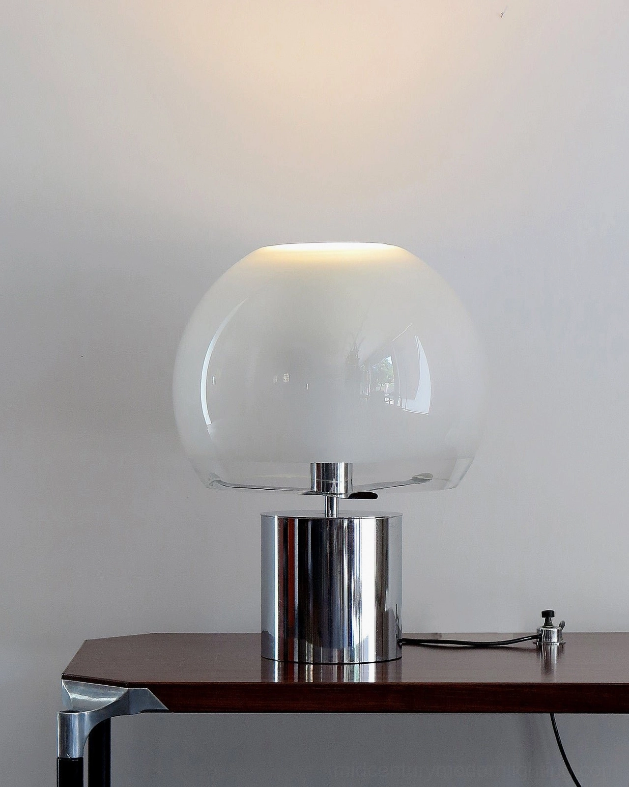Porcino Table Lamp with chrome base on wooden side table, low angle perspective showing modern minimalist design