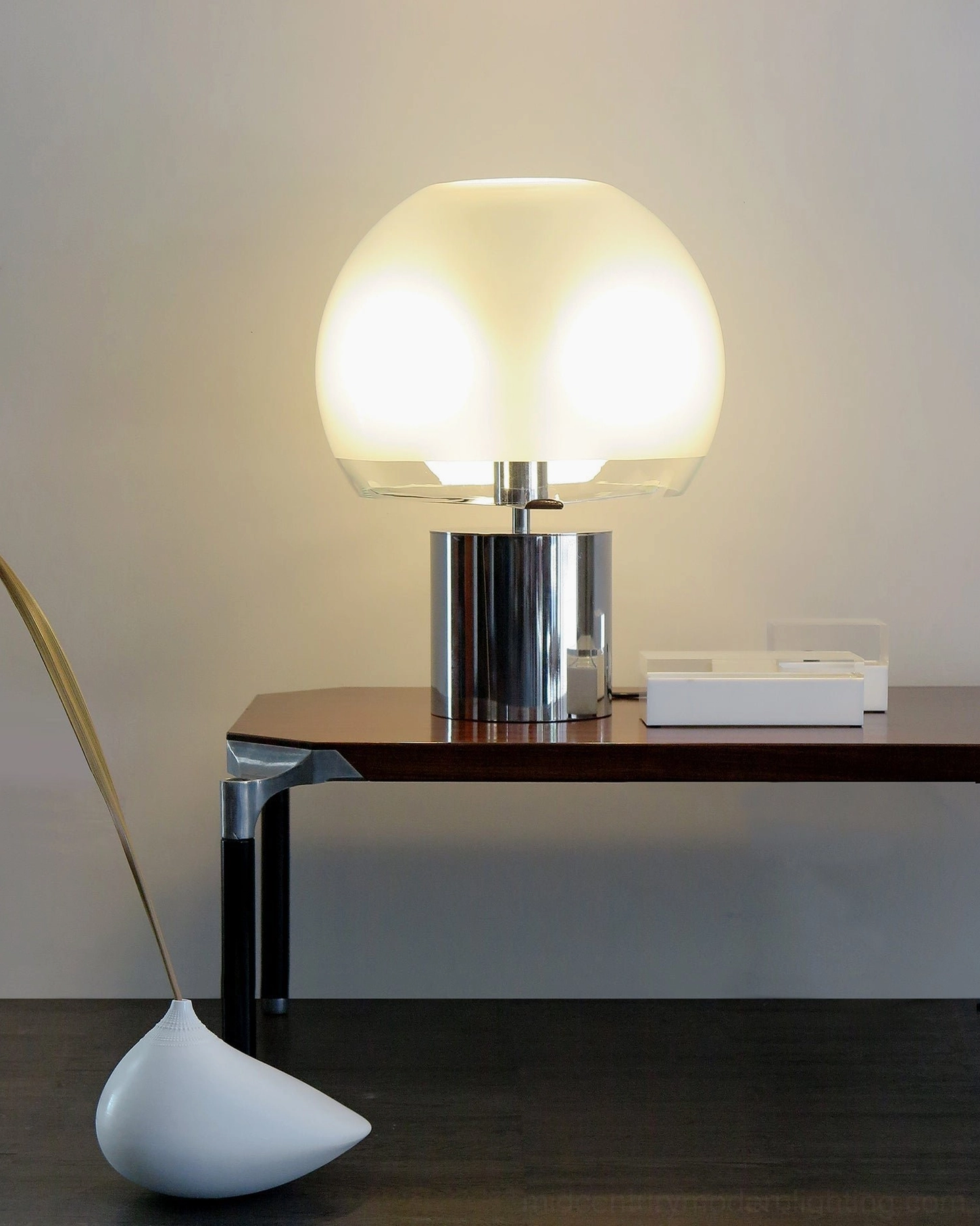 Porcino chrome base table lamp with frosted glass sphere on narrow wooden side table paired with minimalist decorative ornaments