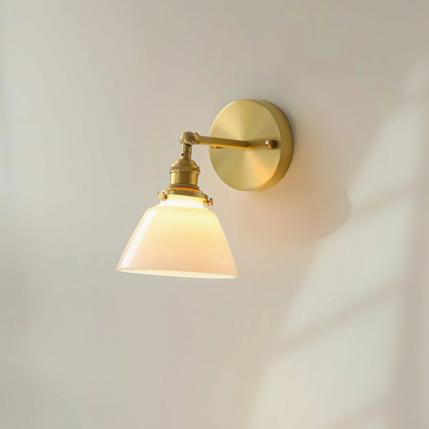 Portland swivel sconce mounted on interior wall with soft shadow detail, brass fixture with lit frosted shade