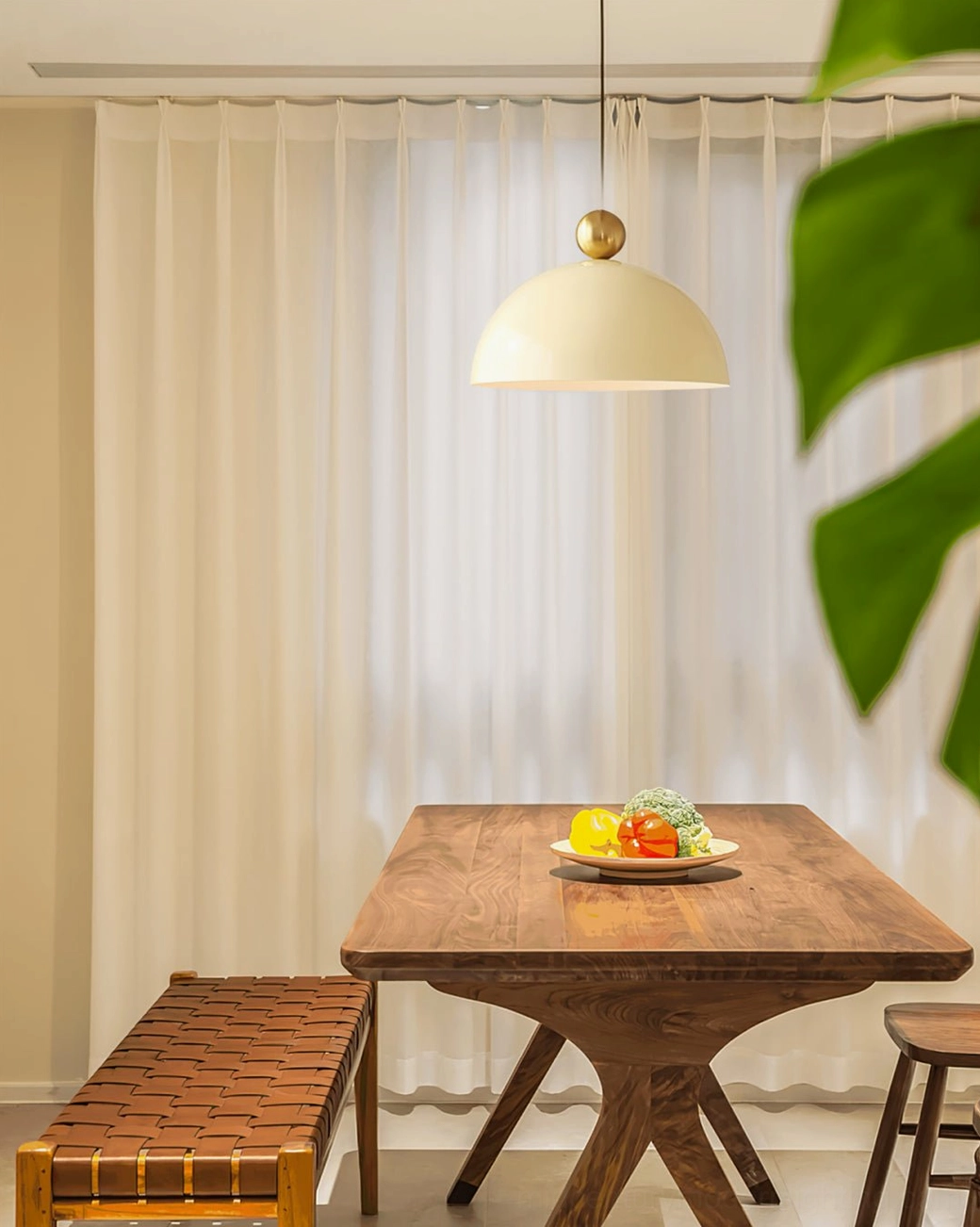 Cream dome pendant lamp suspended over wooden dining table in warm interior lighting