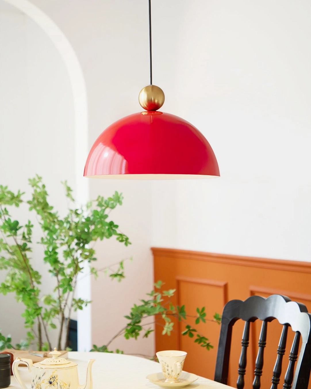 Bright red dome pendant lamp with brass spherical accent in cozy dining area with green plants