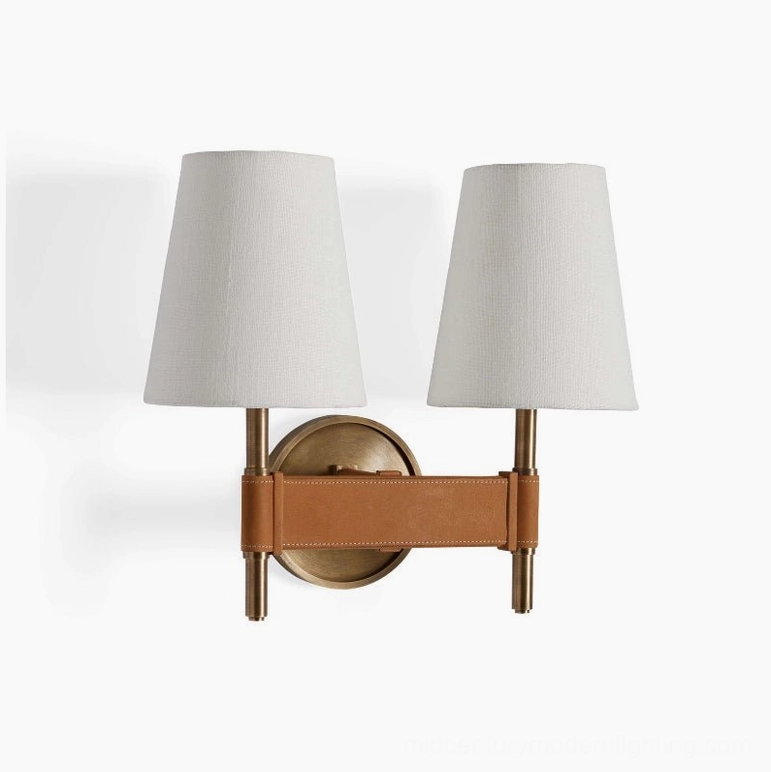 Front-facing view of Prescot dual-head wall sconce with symmetrical arms, neutral off-white shades, and matching tan leather and brass accents