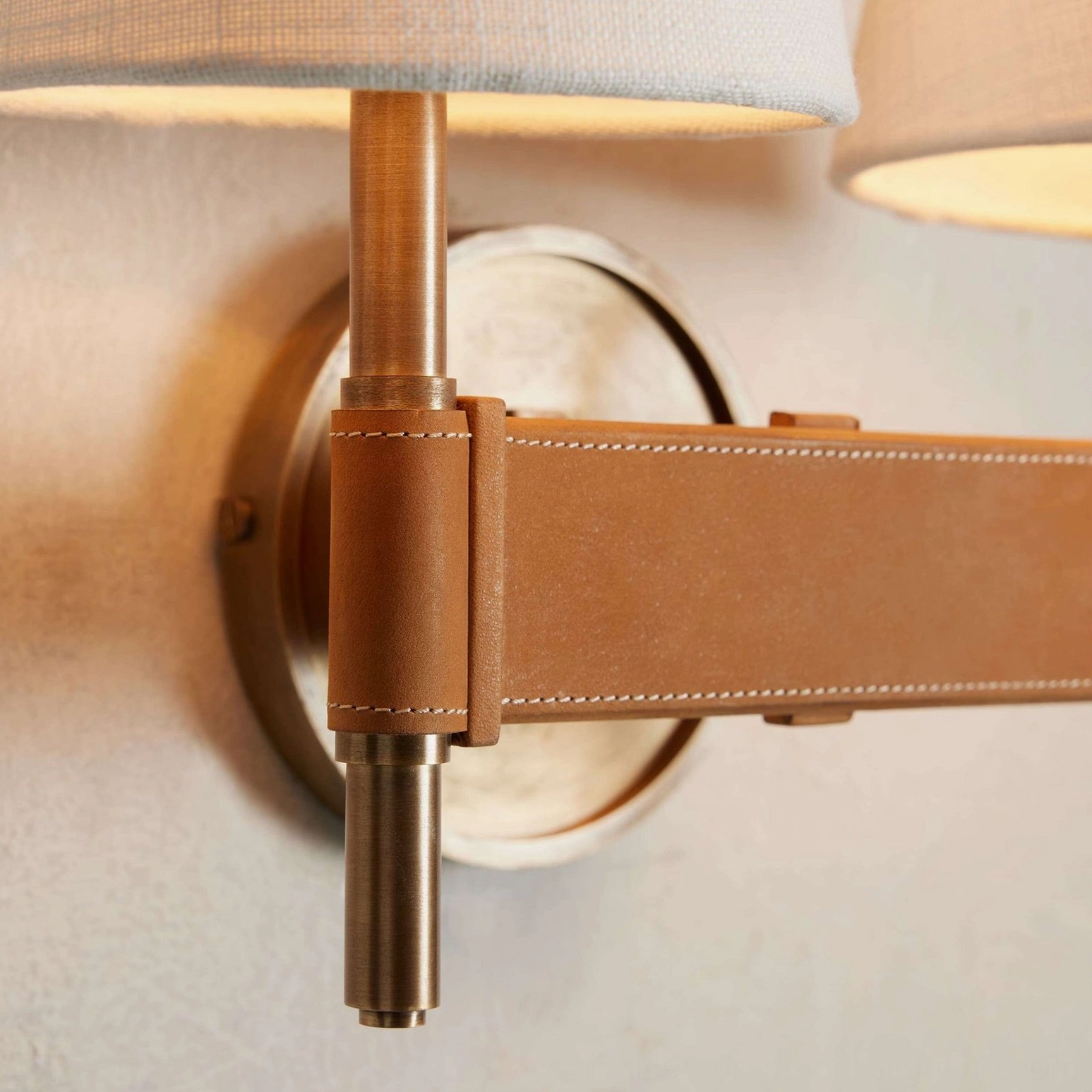 Detailed view of Prescot dual-head sconce highlighting hand-stitched leather crossbar and brushed brass backplate construction