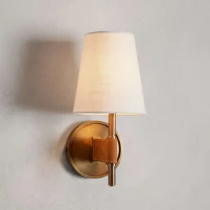 Close-up detail of Prescot wall sconce mounted on textured wall with warm ambient lighting, showcasing leather stitching and brass elements
