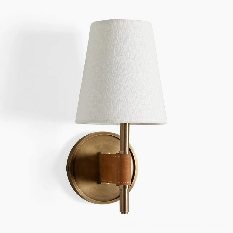 Low-angle studio view of Prescot single wall sconce featuring round brass backplate, leather strap fixture, and tapered fabric shade