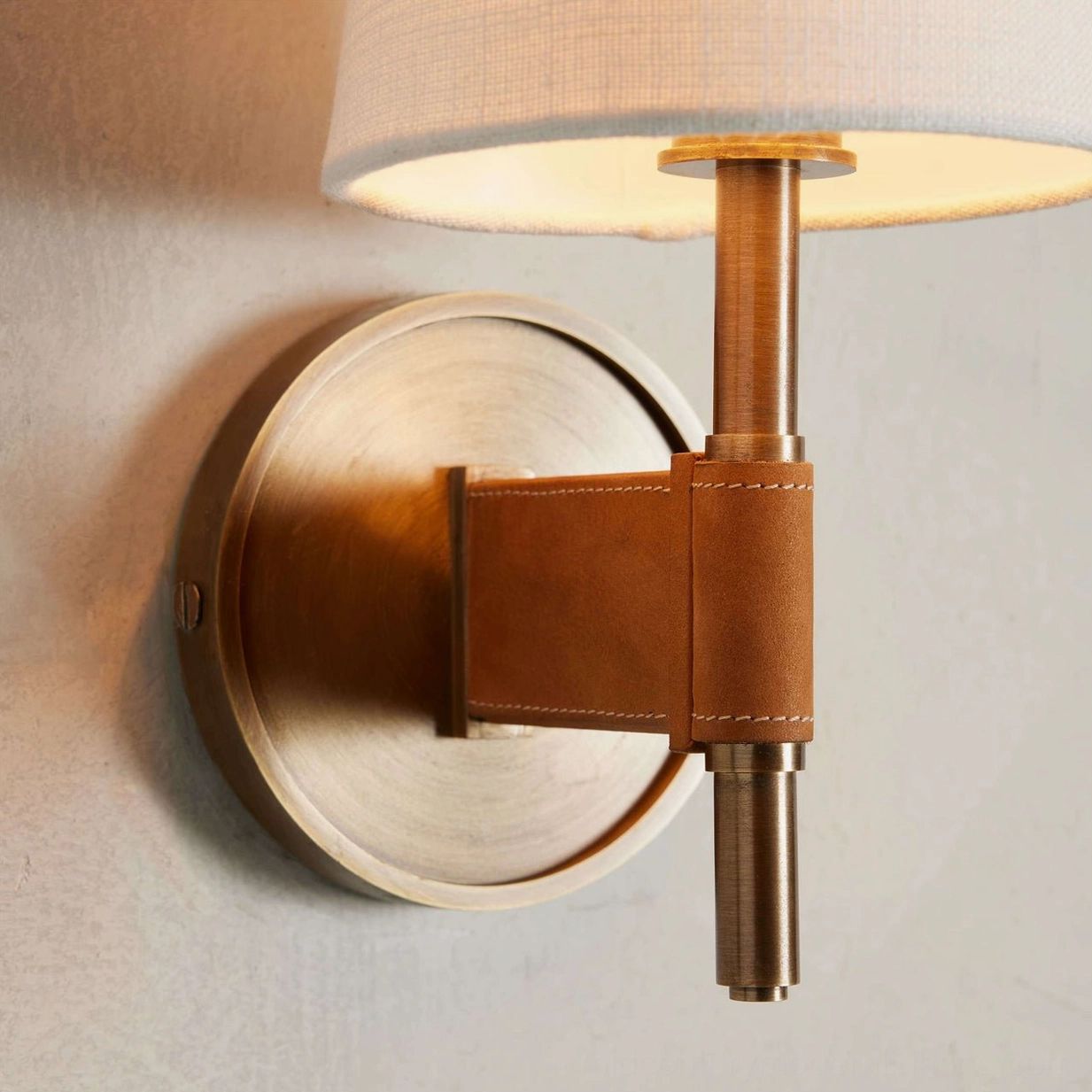 Overhead detail of Prescot wall sconce showing exposed brass stem, hand-stitched leather fixture, and illuminated fabric shade