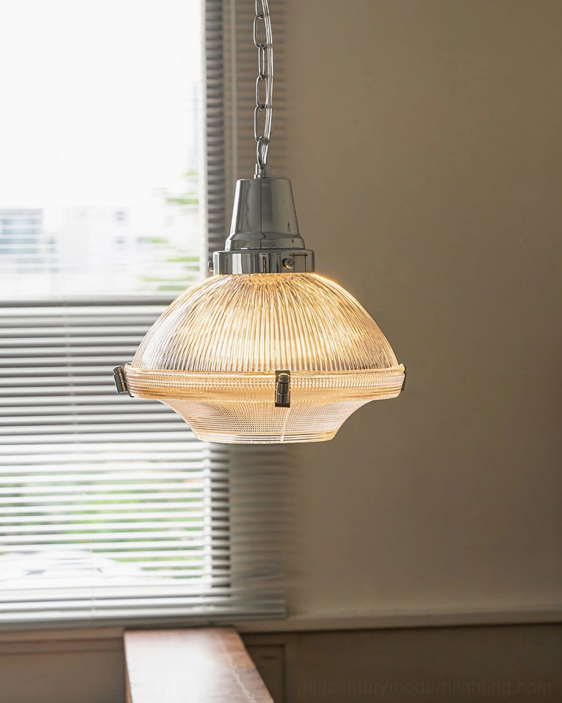 Illuminated ribbed pendant light with warm glow suspended in sunlit dining nook near window
