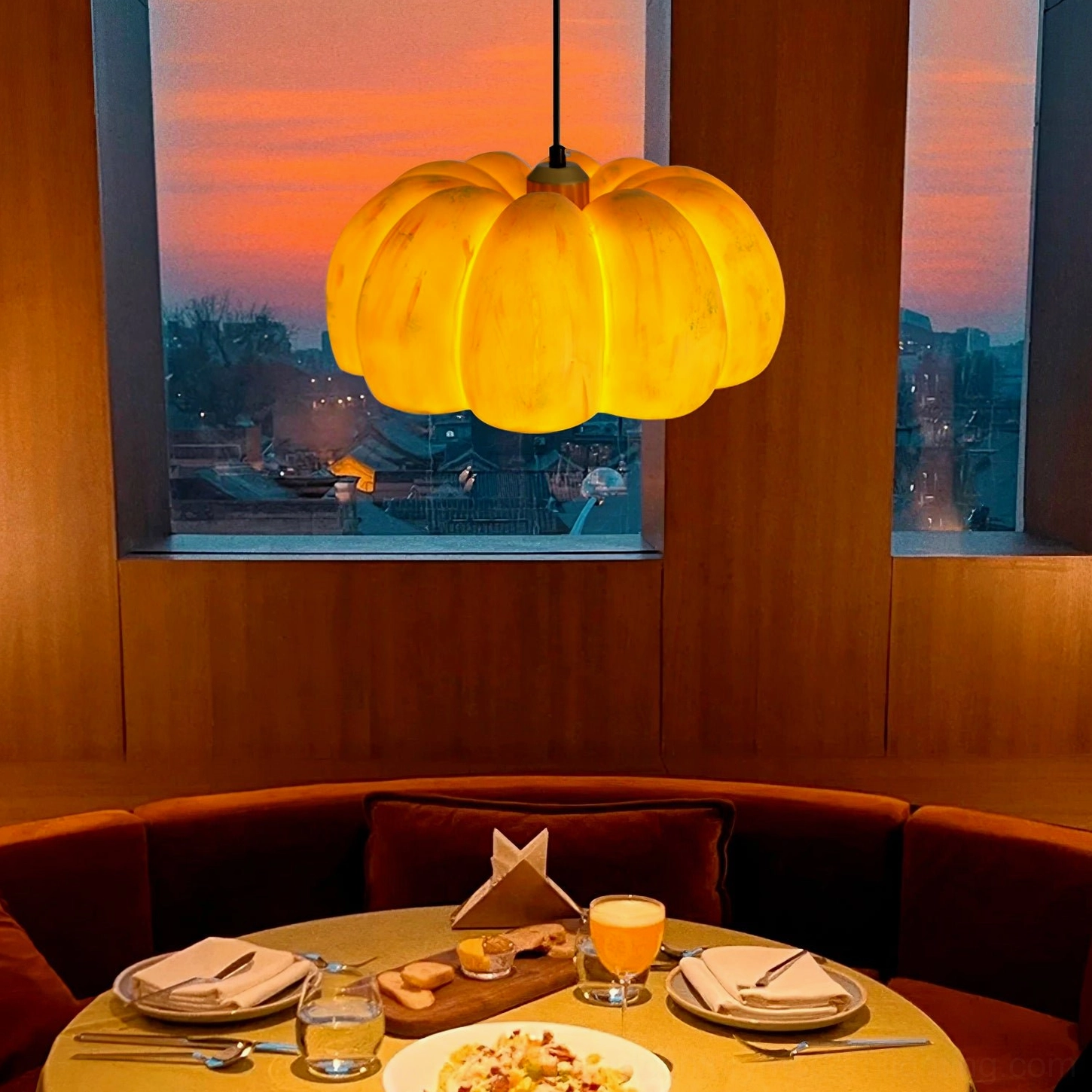 Pumpkin pendant light glowing warm amber in restaurant dining booth with wooden interior and sunset backdrop