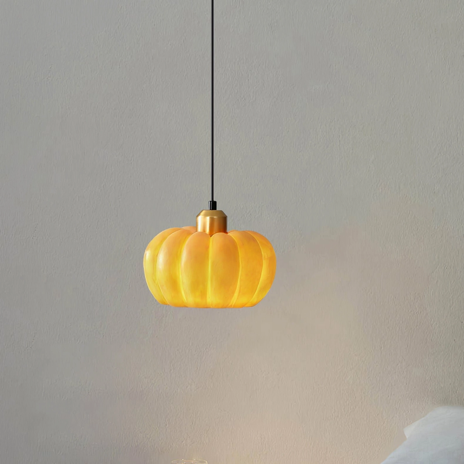Side view of small pumpkin pendant lamp with brass hardware and warm amber color on light gray wall