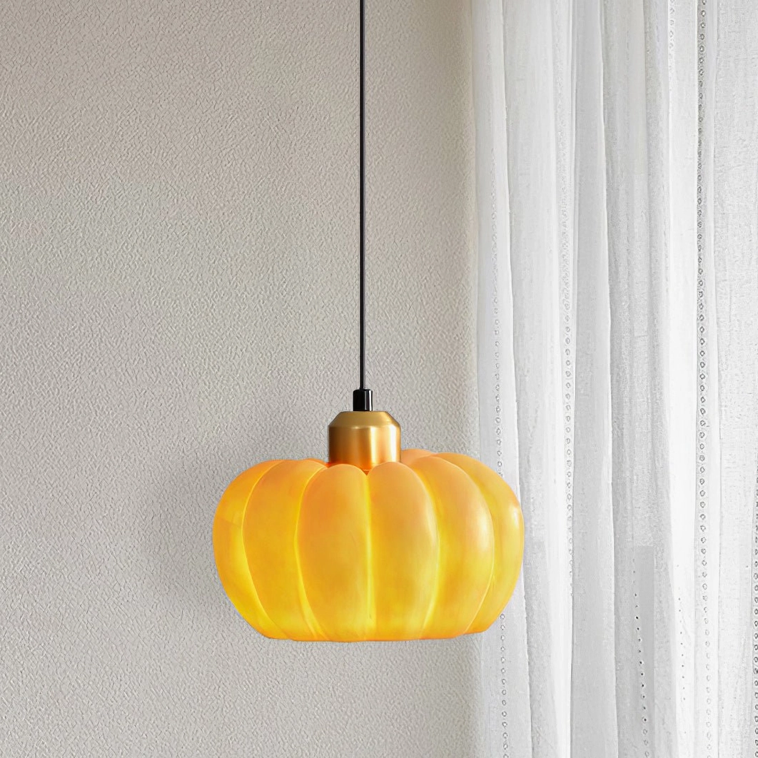 Pumpkin pendant lamp with brass accent top and warm orange shade on white wall background