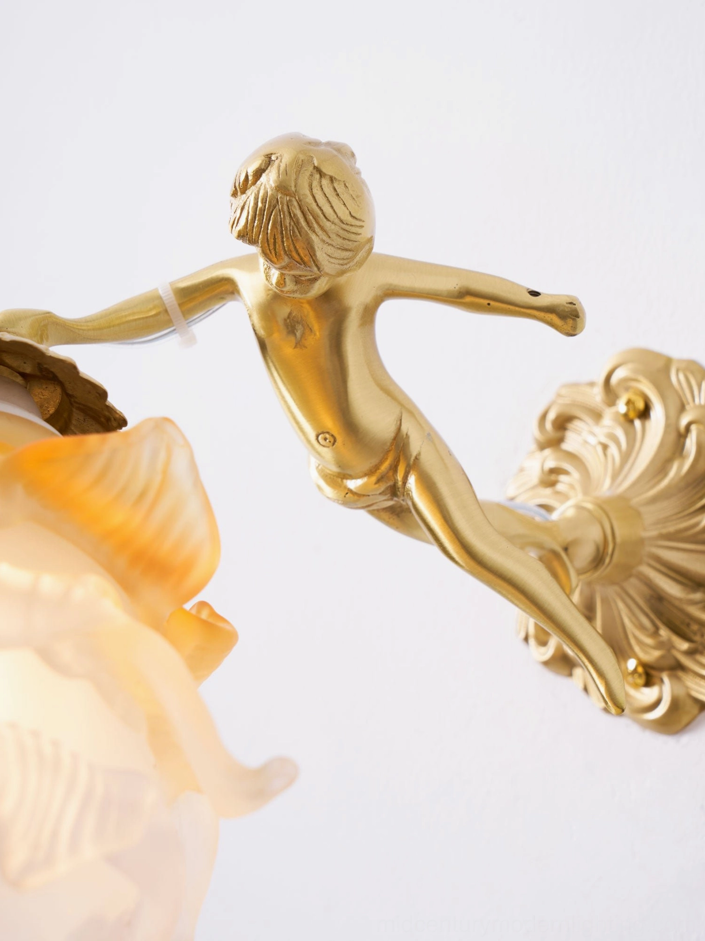 Putti brass wall sconce close-up showing frosted white glass flower petals with yellow detailing and sculptural brass cherub angel figure