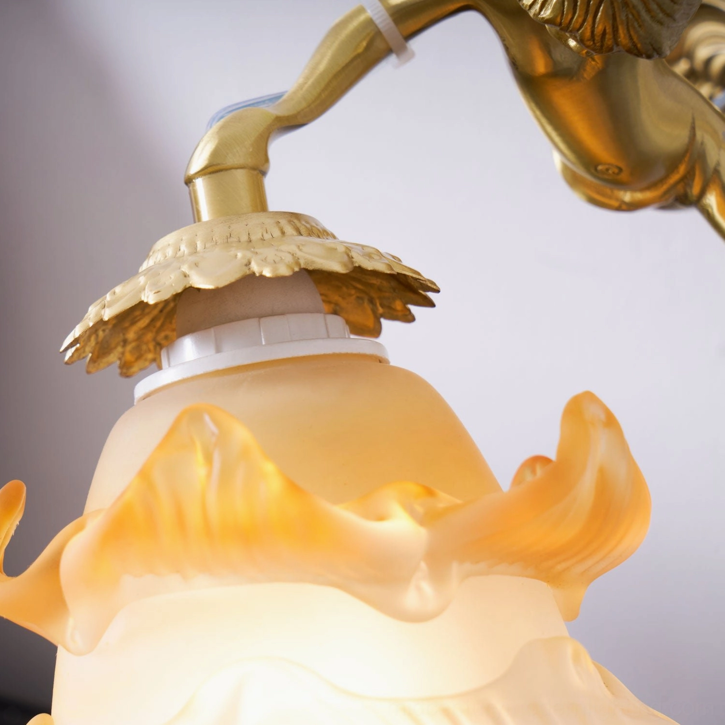 Putti brass wall sconce showing complete fixture assembly with frosted white petal glass shade, modeled cherub figure, and ornate brass shell backplate detail