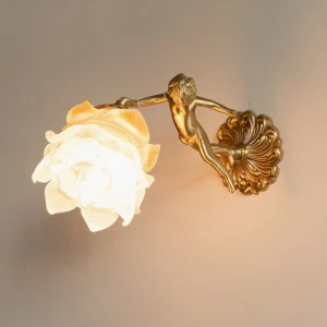 Single putti cherub wall lamp mounted on home interior wall, showing frosted glass flower shade illuminated with warm light, brass angel sculpture detail
