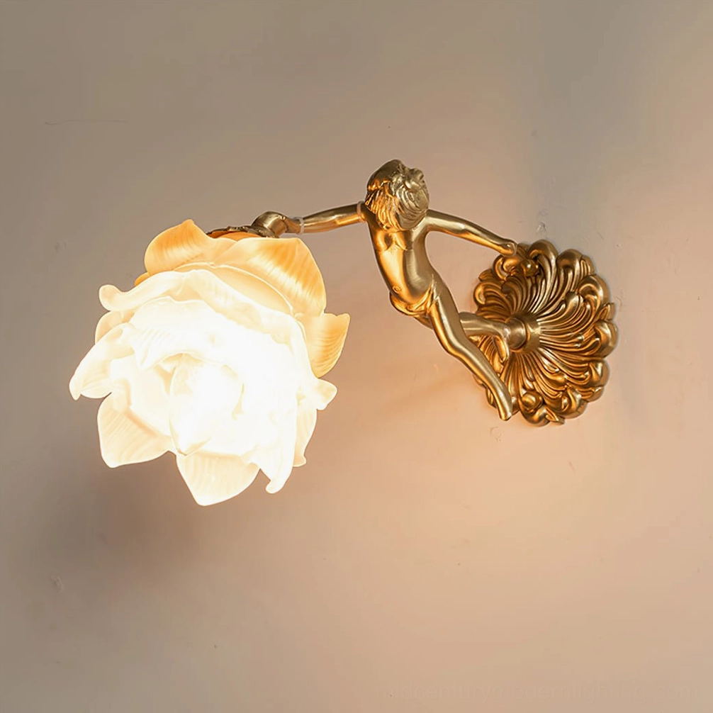 Single putti cherub wall lamp mounted on home interior wall, showing frosted glass flower shade illuminated with warm light, brass angel sculpture detail