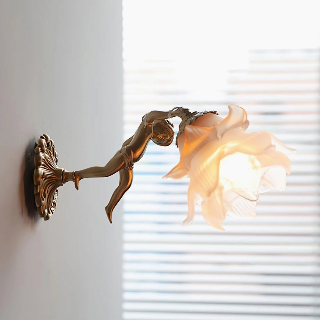Close-up detail of putti cherub wall lamp mounted on home wall, glowing frosted flower glass shade with yellow petal accents, compact brass fixture