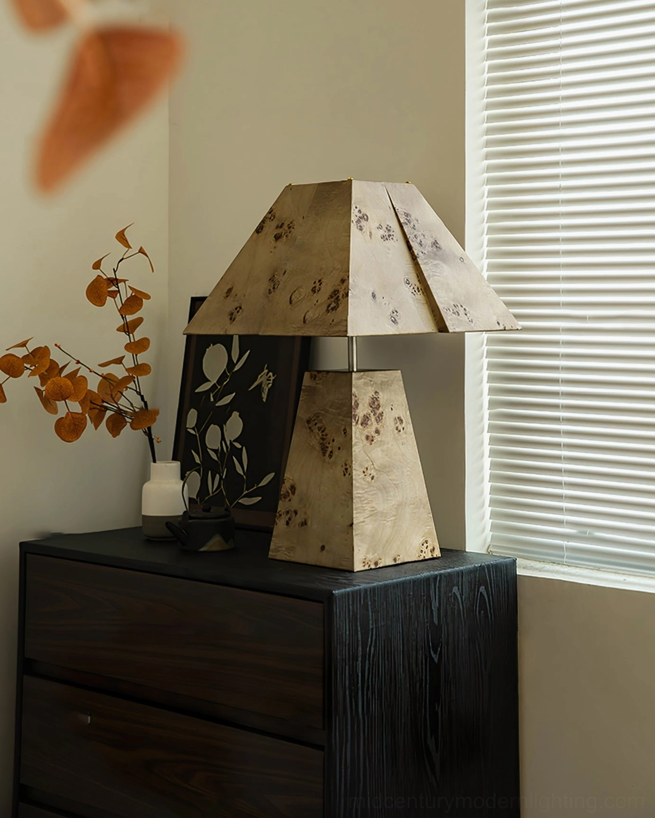 Pyramid wood table lamp on dark wood bedside table with sheer curtains, warm glow at night