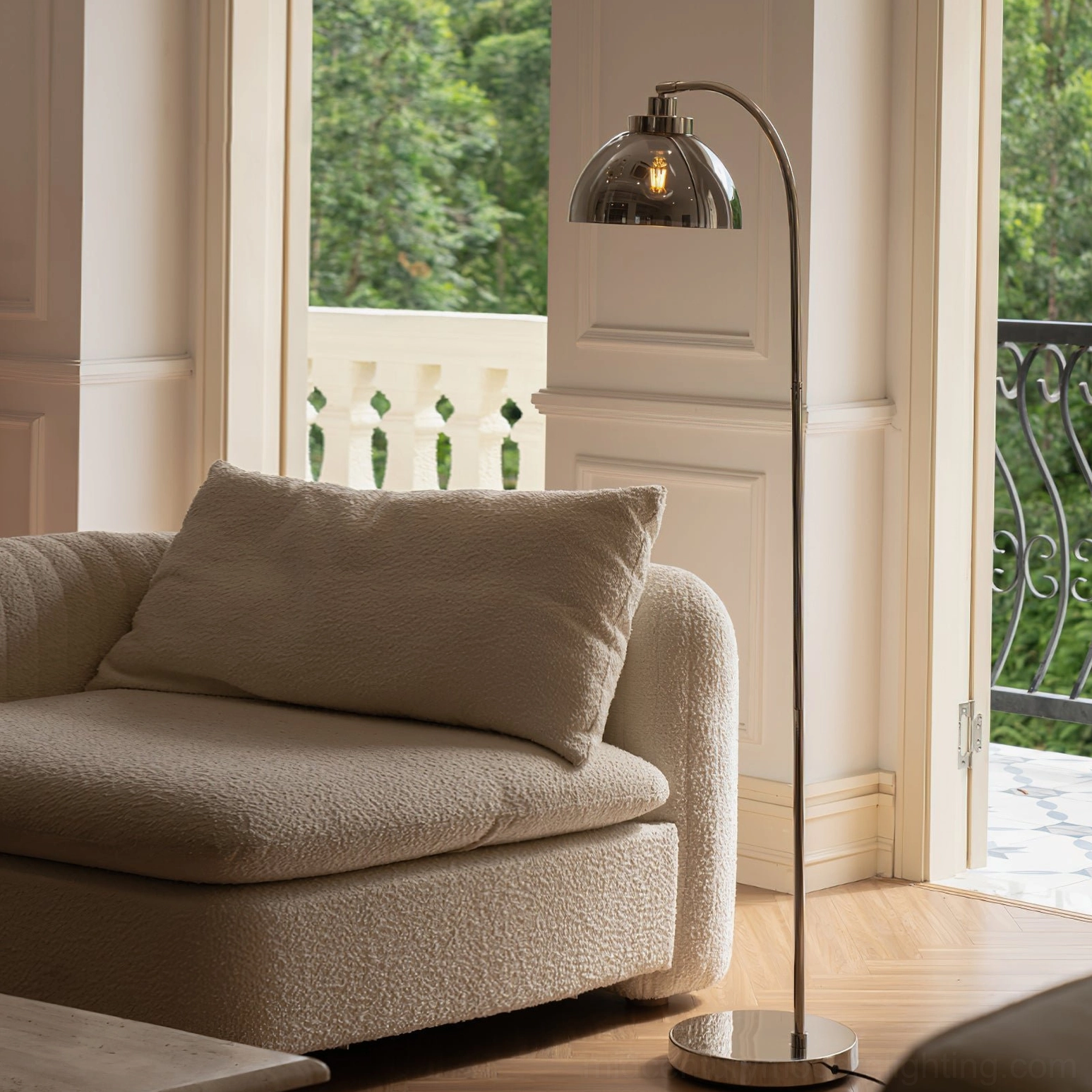 Sculptural arc floor lamp beside boucle sofa in sunlit living room with balcony view