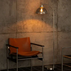 Mid-century modern arc lamp positioned in industrial loft beside leather chair with concrete wall backdrop