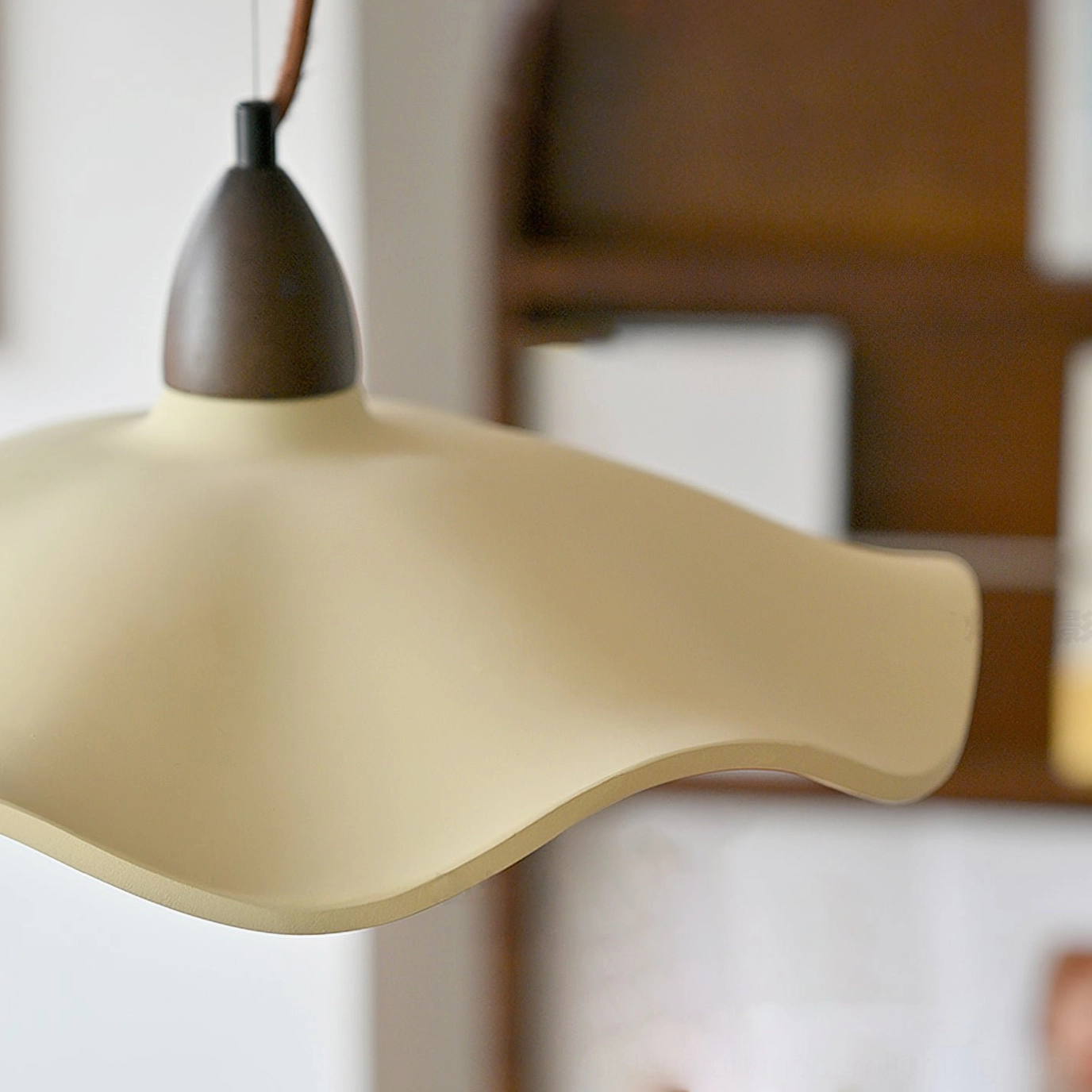 Close-up detail of Radha wave pendant showing smooth matte beige cement texture and dark walnut wood fixture