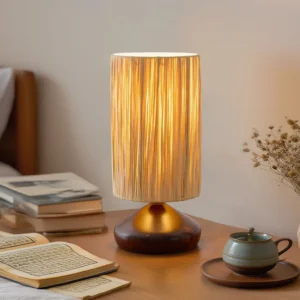 Warm glowing raffia table lamp on bedroom nightstand with books and tea set, japandi bedroom decor styling
