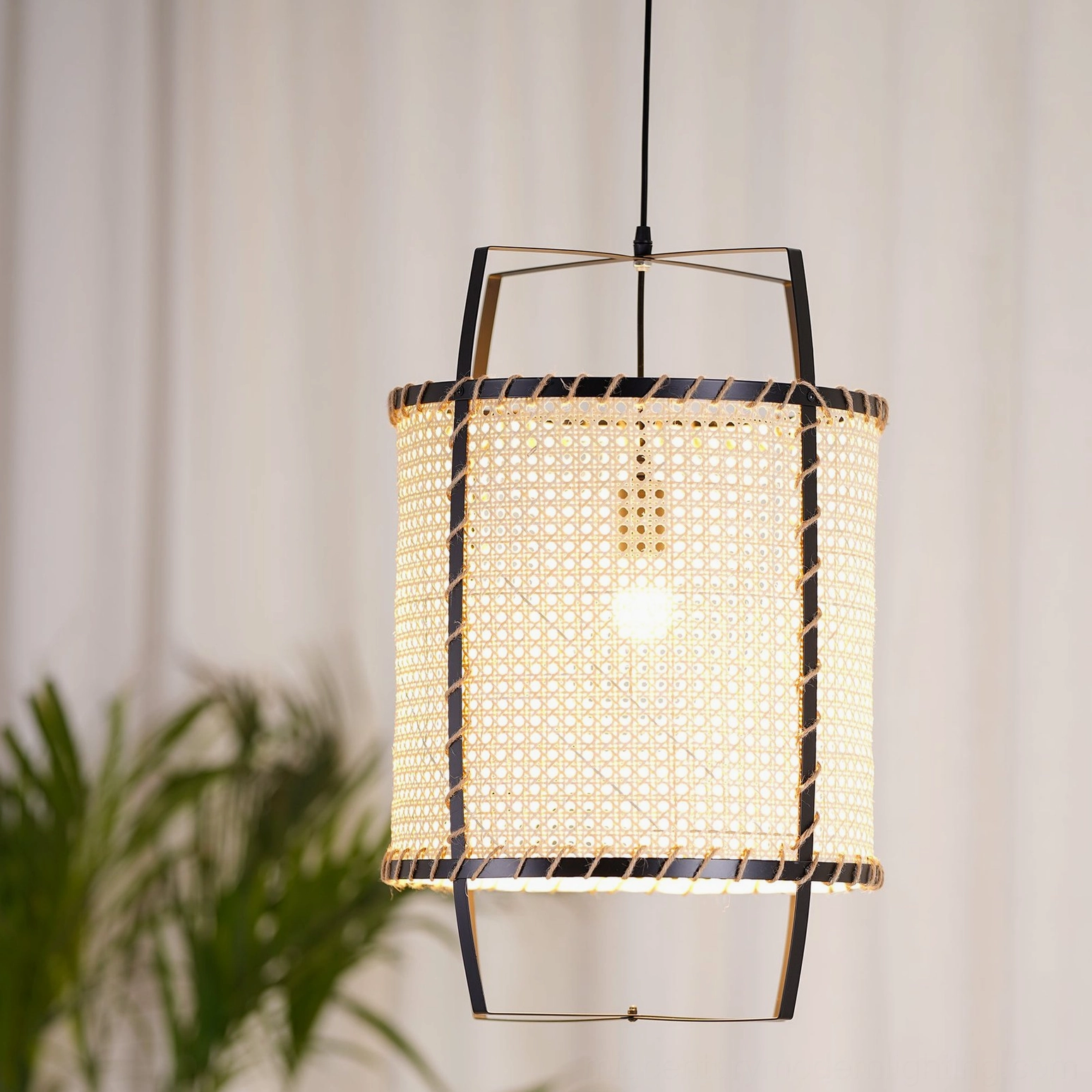 Rattan cane pendant light in contemporary interior setting, capturing sculptural cylindrical silhouette and warm diffused lighting through perforated weave