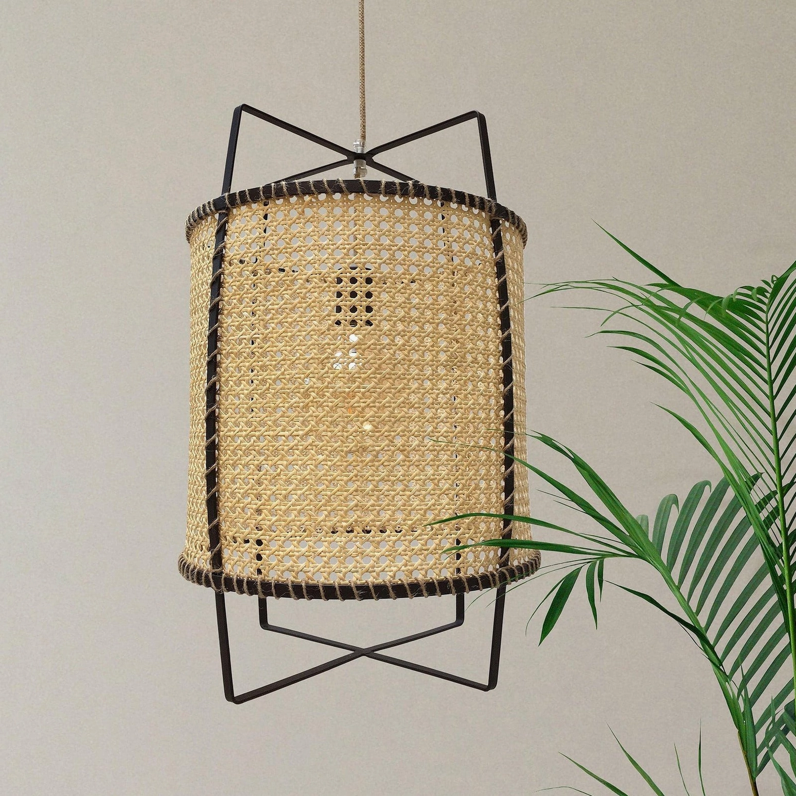 Mid-century modern rattan cane suspension light, close-up side view showing cylindrical geometric open frame and tightly woven natural rattan mesh