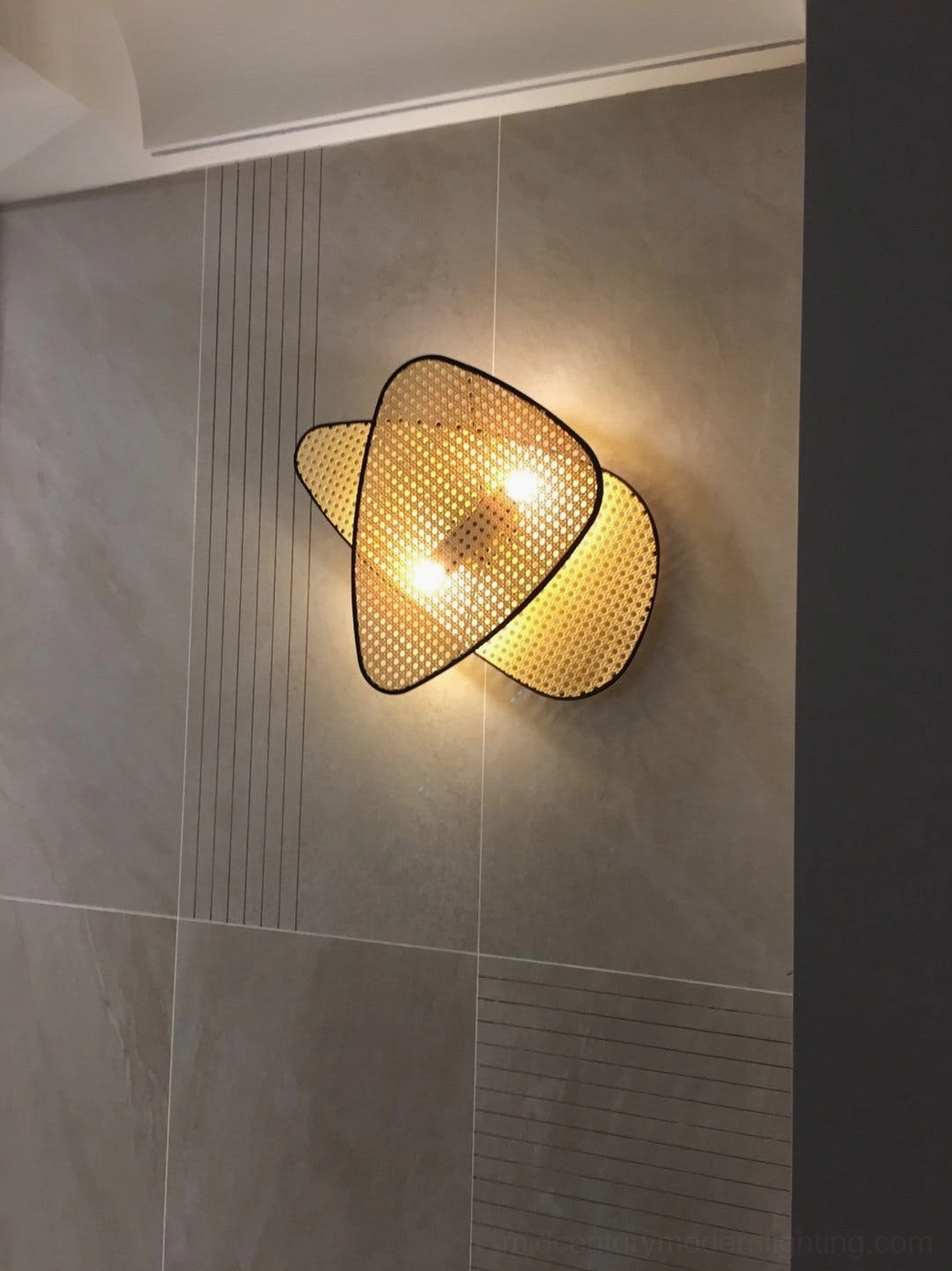Rattan woven wall lamp side view on grey striped wall displaying natural rattan texture and warm ambient illumination