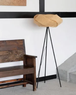 Rattan tripod floor lamp displayed in entryway with vintage wooden bench, three-quarter view showing warm natural rattan weave