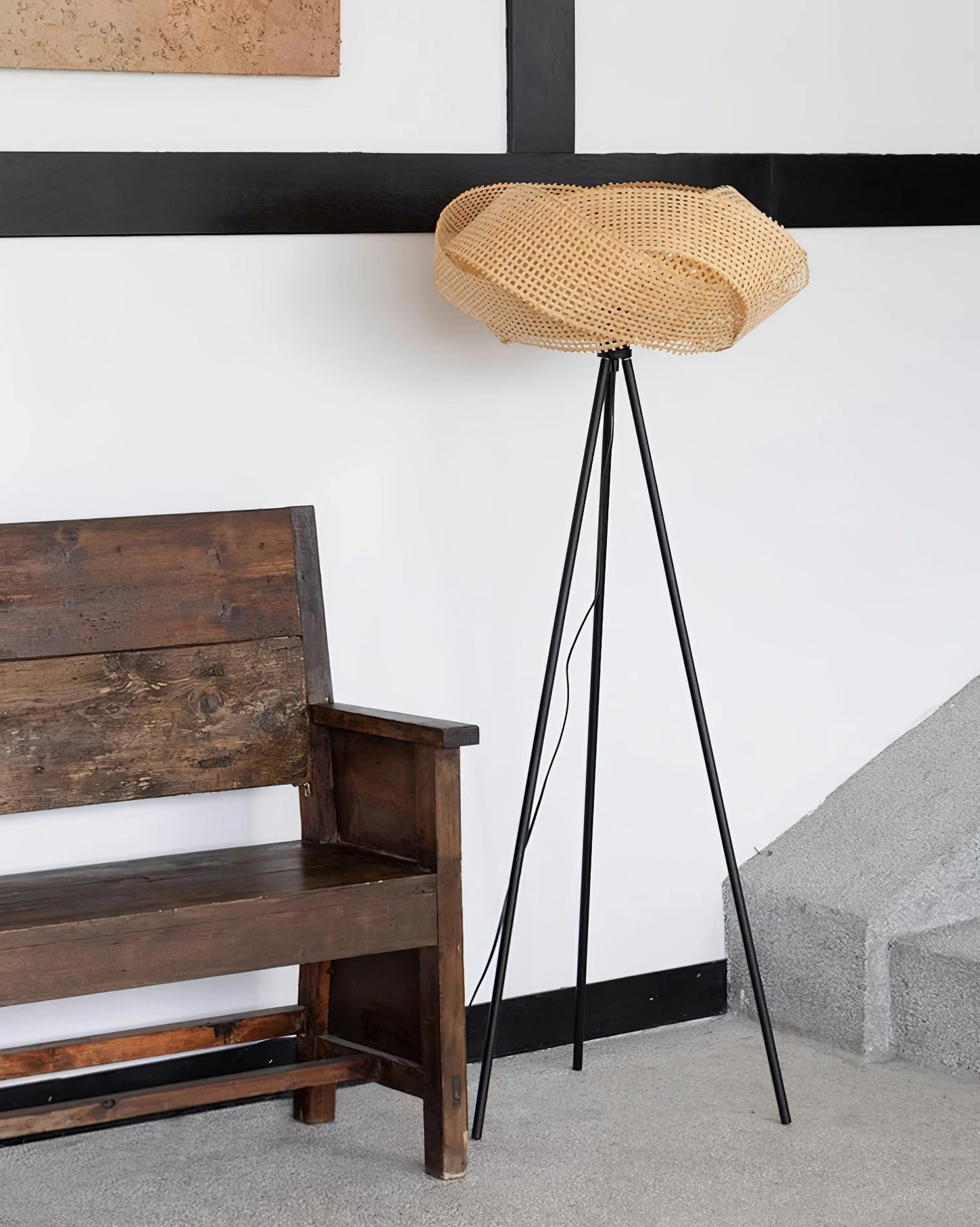 Rattan tripod floor lamp displayed in entryway with vintage wooden bench, three-quarter view showing warm natural rattan weave