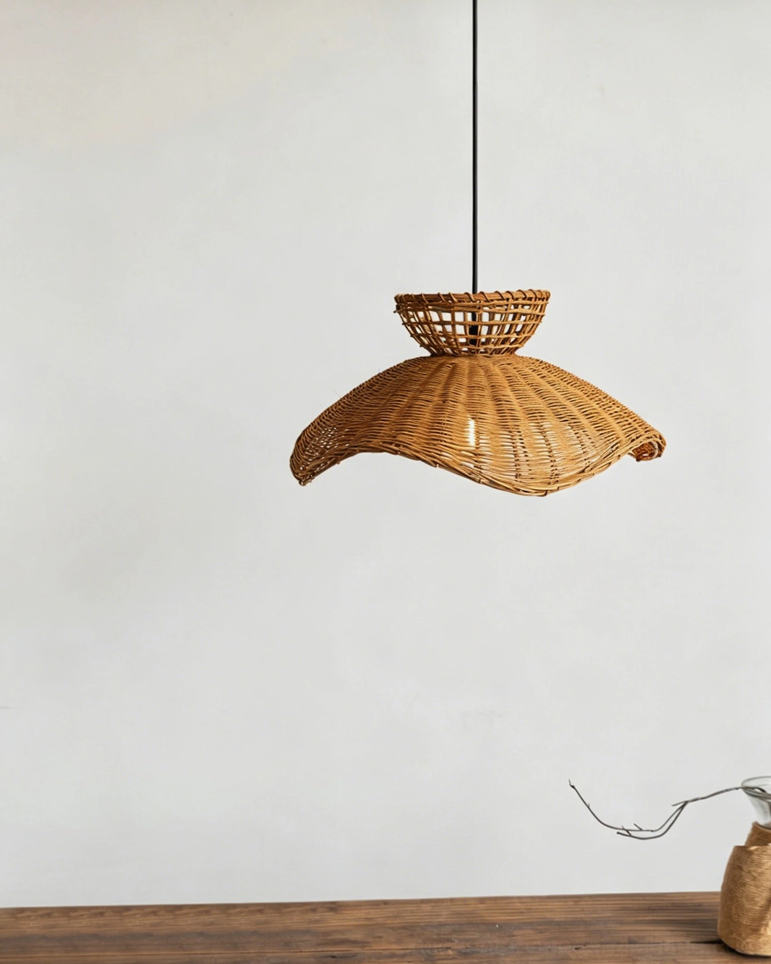 Low angle side view of handwoven rattan pendant shade with curved wavy edges and natural brown finish