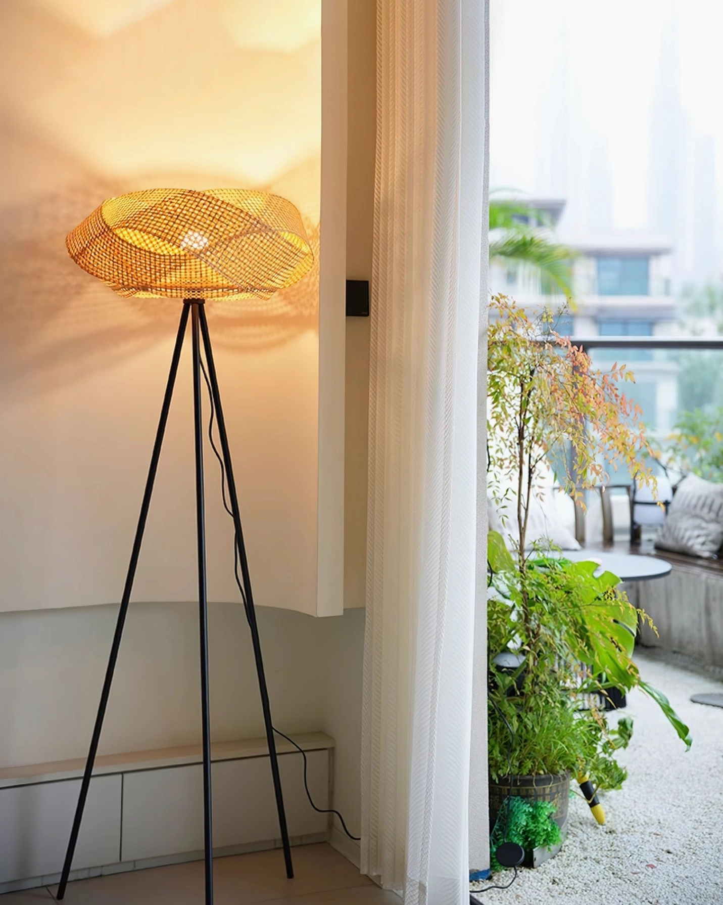 Rattan tripod floor lamp on indoor balcony space with warm glowing ambient light, three-quarter frontal view for home decor