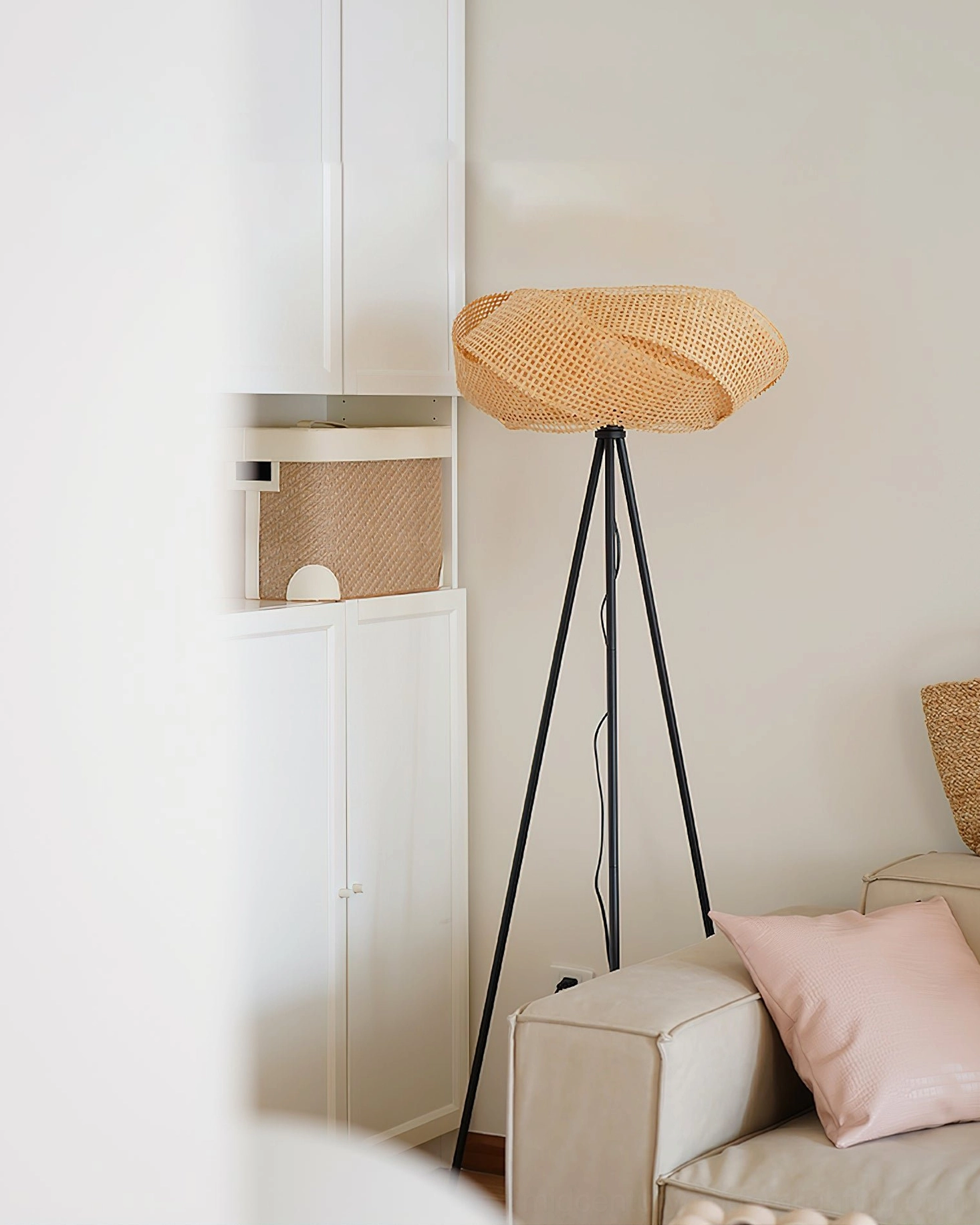Contemporary rattan floor lamp beside modern living room fabric sofa, side perspective view with beige rattan and matte black frame