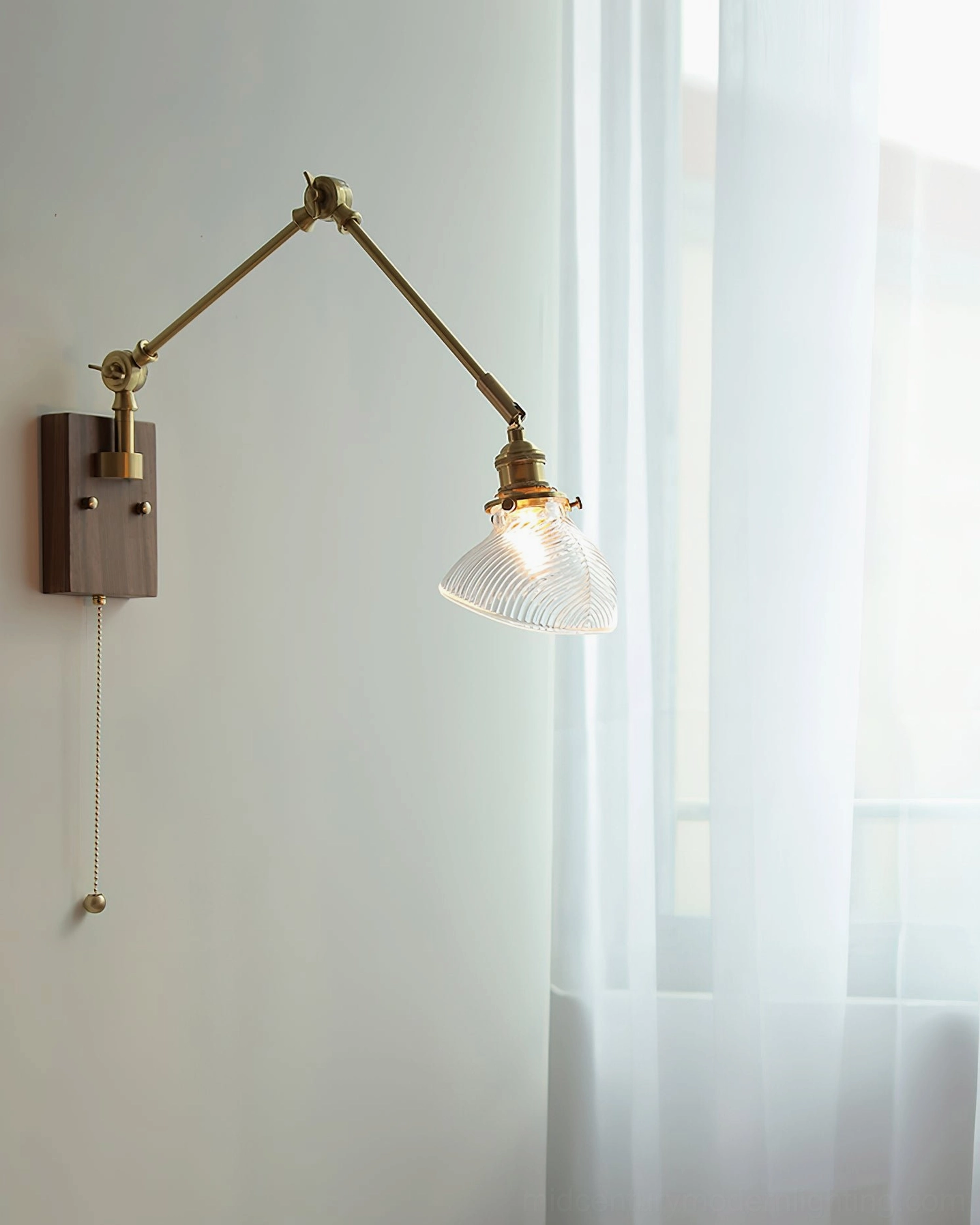 Clear glass ribbed shade swing arm lamp illuminated in bedroom, showing warm light through transparent glass with dark wood mount