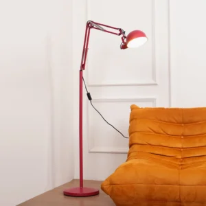 Red floor lamp with articulated swing arm positioned in modern living room next to orange tufted sofa, side angle view