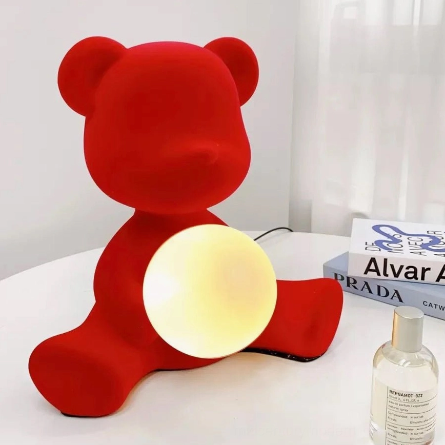 Red teddy bear table lamp glowing on bedroom nightstand with warm yellow light and decorative books