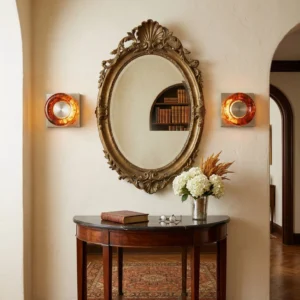 Pair of red wall sconces flanking ornate gilded oval mirror in classic French entryway with console table