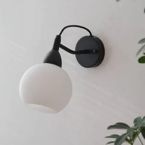 Reese mid-century modern wall sconce three-quarter view mounted on textured wall with decorative greenery
