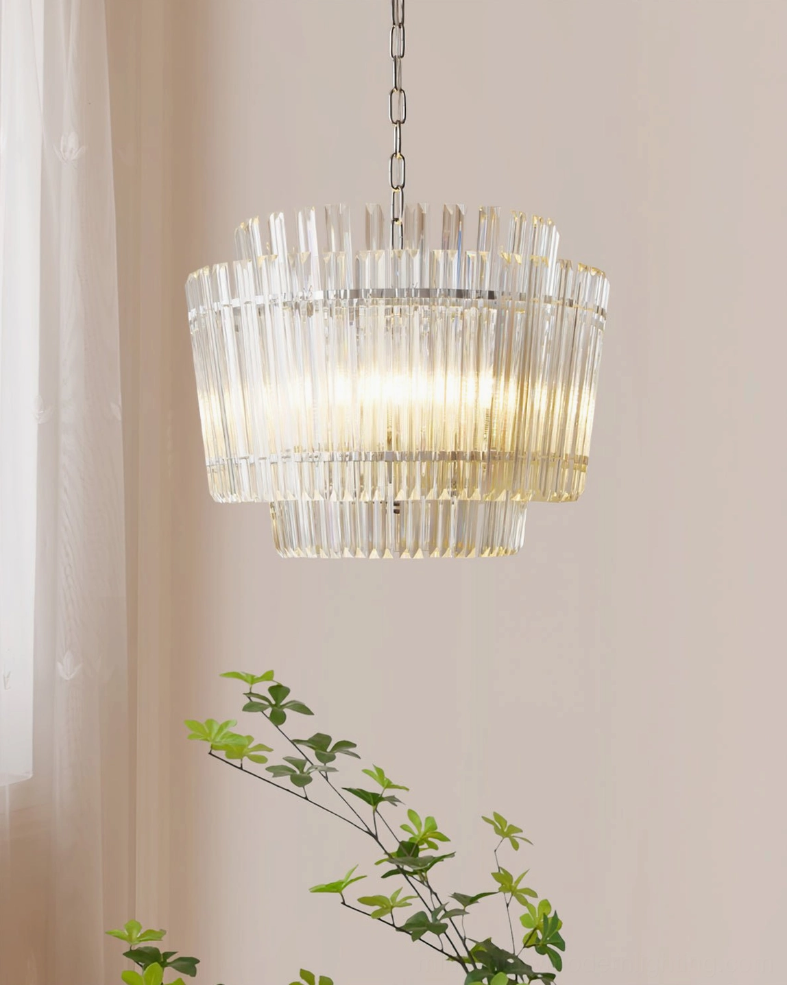 Regina chandelier hanging indoors with warm ambient lighting illuminating cascading glass rods near decorative plants