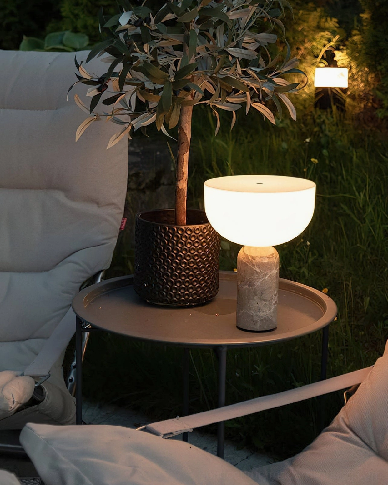 Light brown Rosso Levanto marble base Renard lamp with warm ambient glow on outdoor patio side table