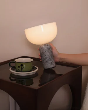 Hand holding cordless Renard marble lamp with gray marble base, warm glowing light in modern living room interior