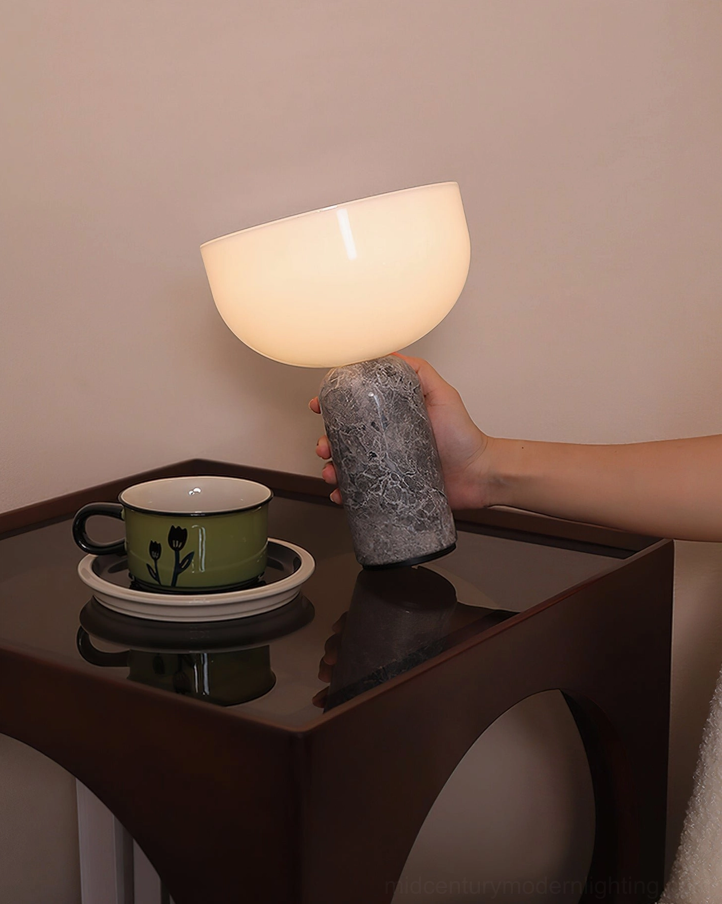 Hand holding cordless Renard marble lamp with gray marble base, warm glowing light in modern living room interior