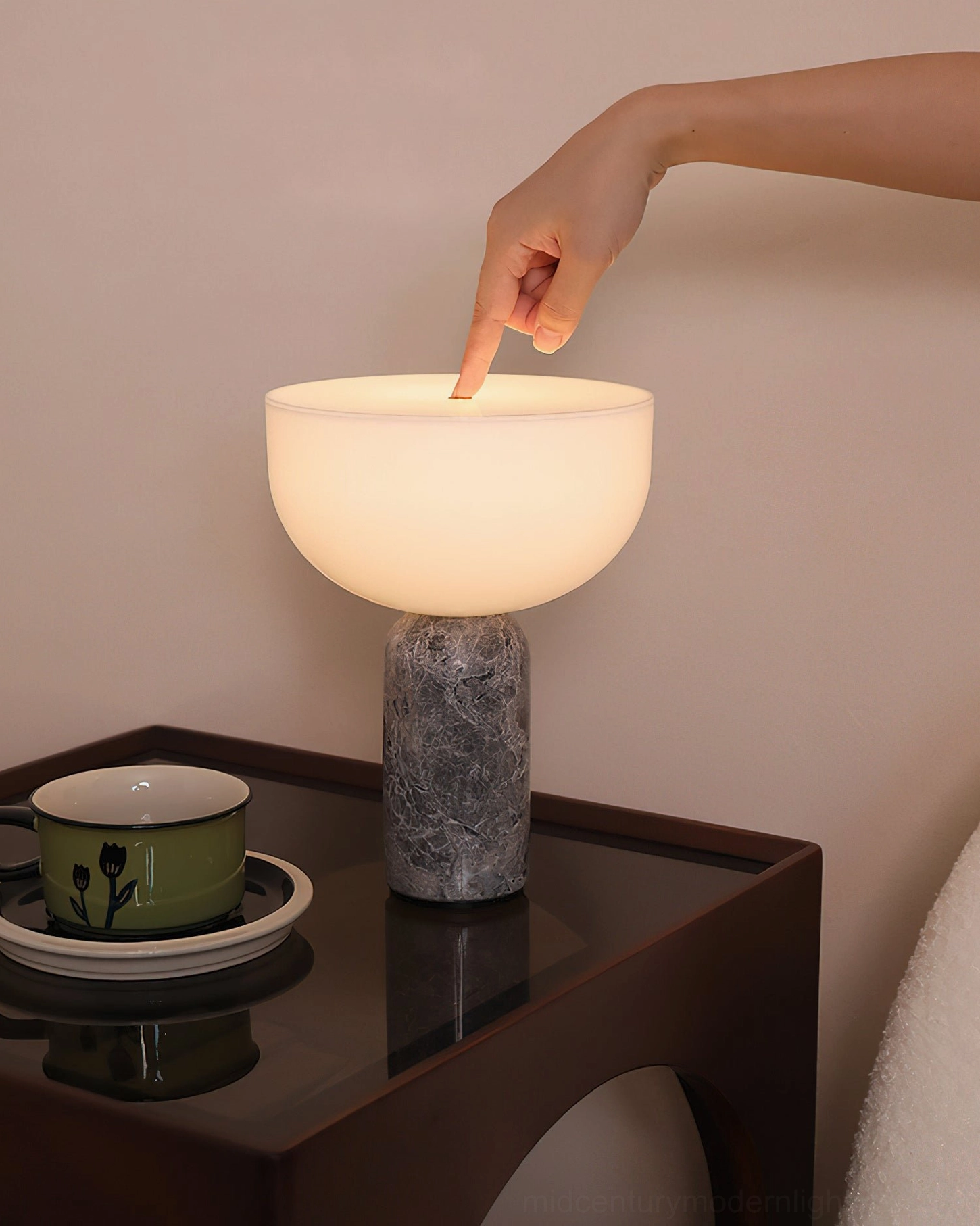 Finger touching frosted glass shade of Renard marble lamp on dark wooden side table with ambient lighting