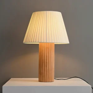 Respira table lamp three-quarter angle view showing ribbed wooden base and warm ambient lighting on concrete platform