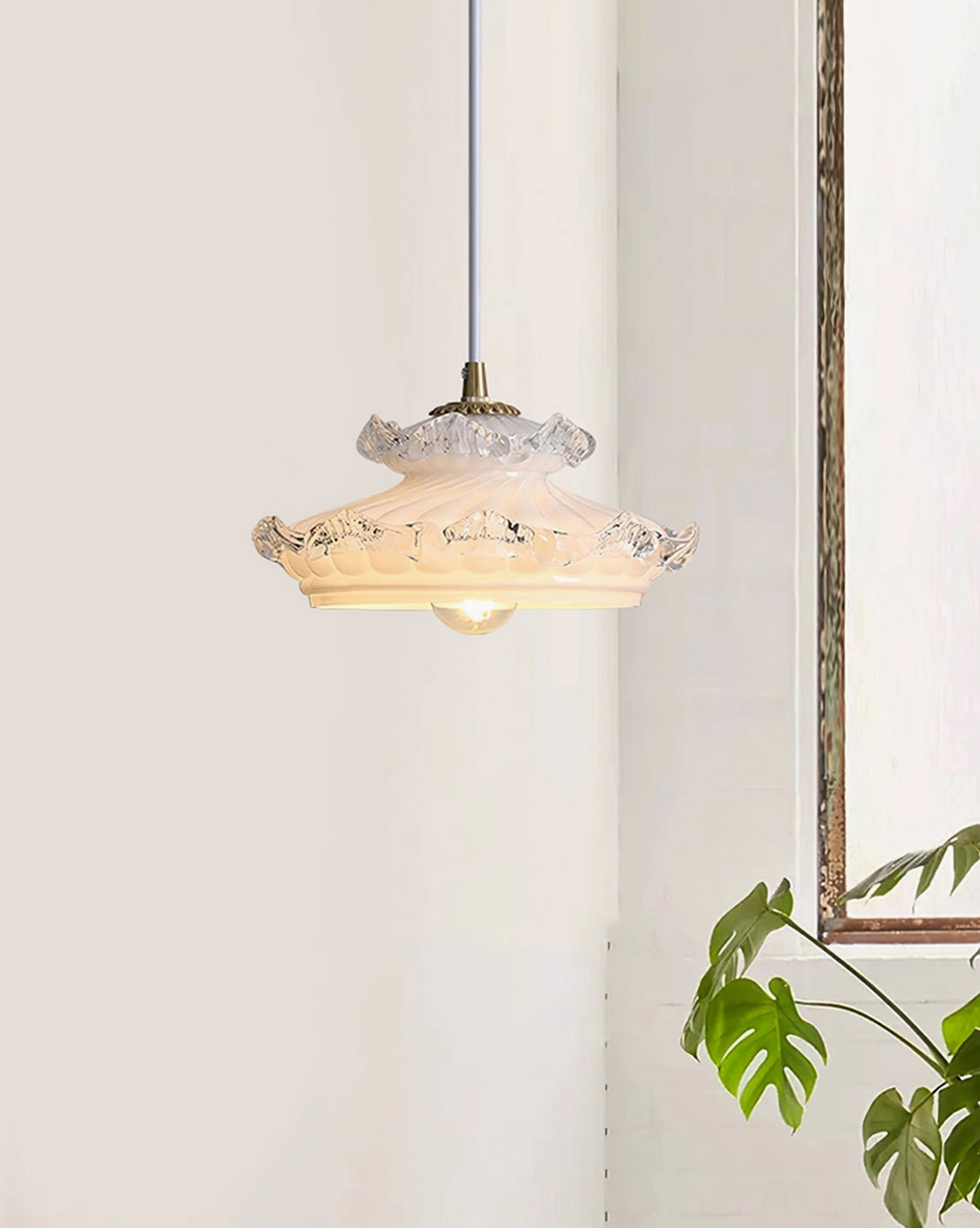 Cream milk glass pendant light with gold metal fixtures and green potted plant in minimalist room