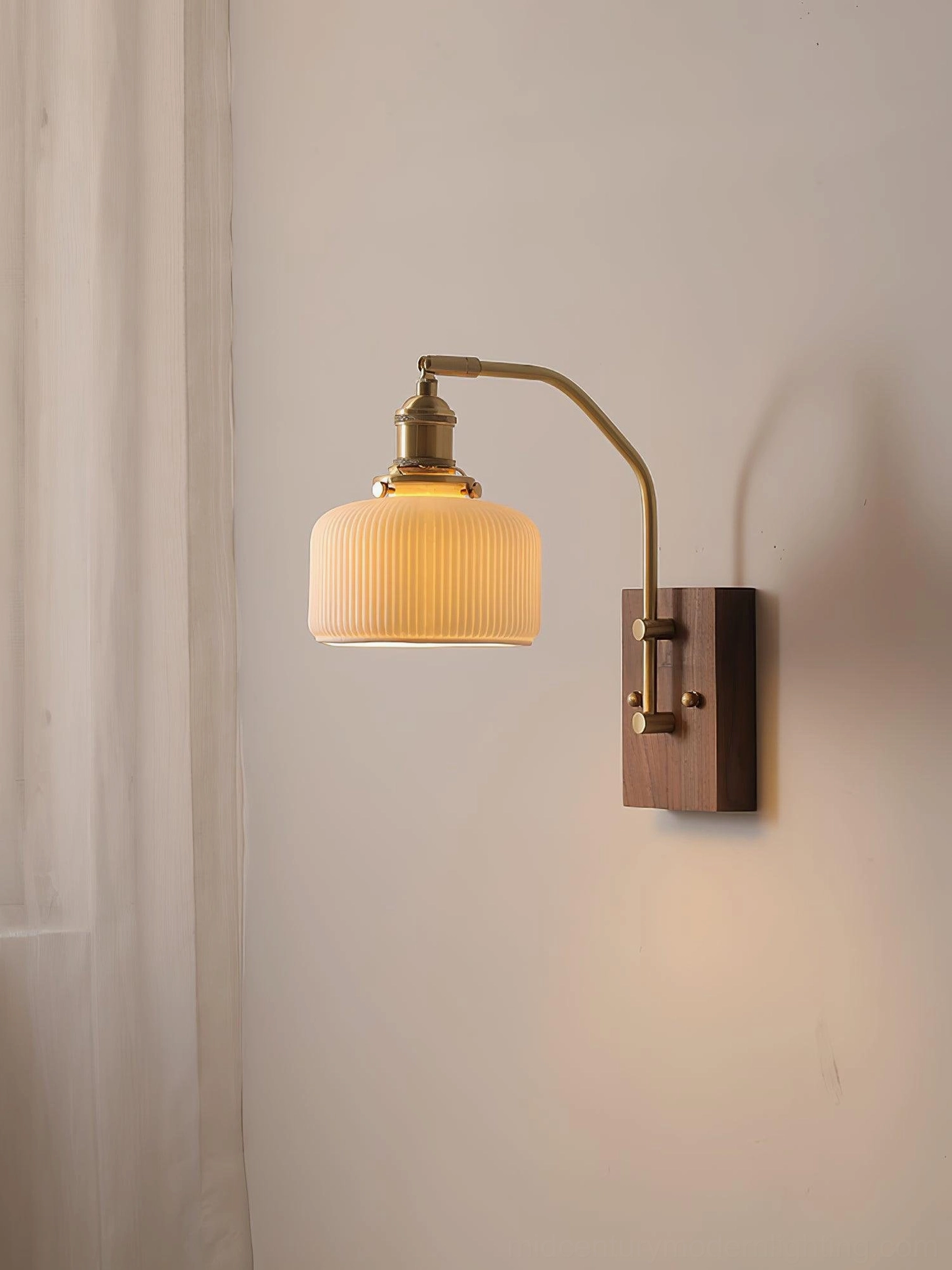 Retro wall sconce with short cylinder ribbed shade and curved brass arm against indoor wall with curtain