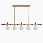 Reya linear chandelier with 5 glass globe shades in brass gold and walnut wood, front studio view showing mid-century modern design details