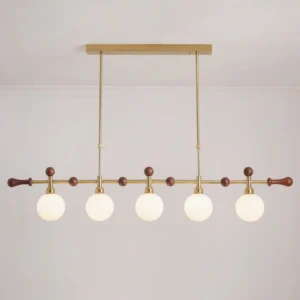 Lit Reya linear chandelier with warm white illumination, brass metal framework and opal glass globes creating ambient dining light
