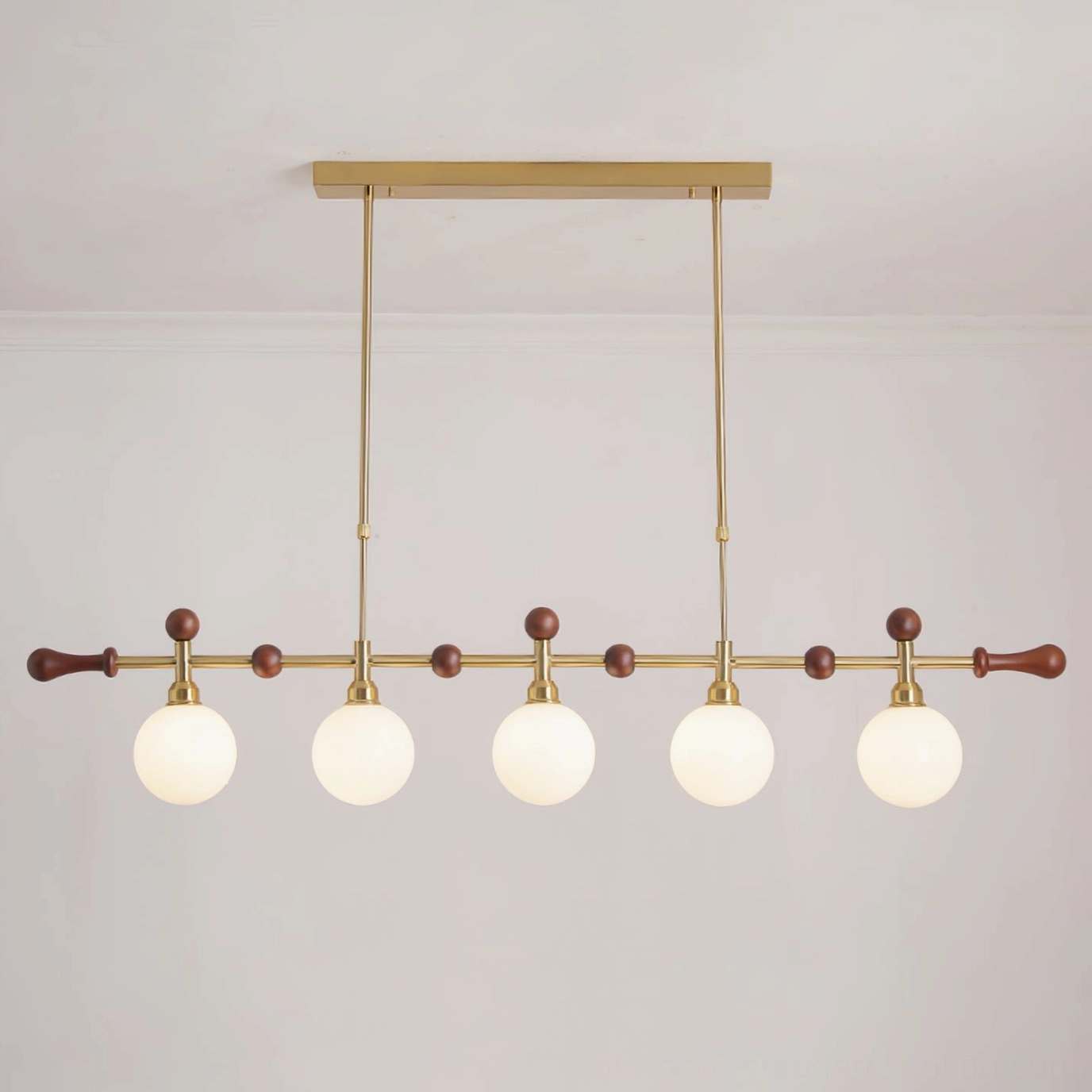 Lit Reya linear chandelier with warm white illumination, brass metal framework and opal glass globes creating ambient dining light