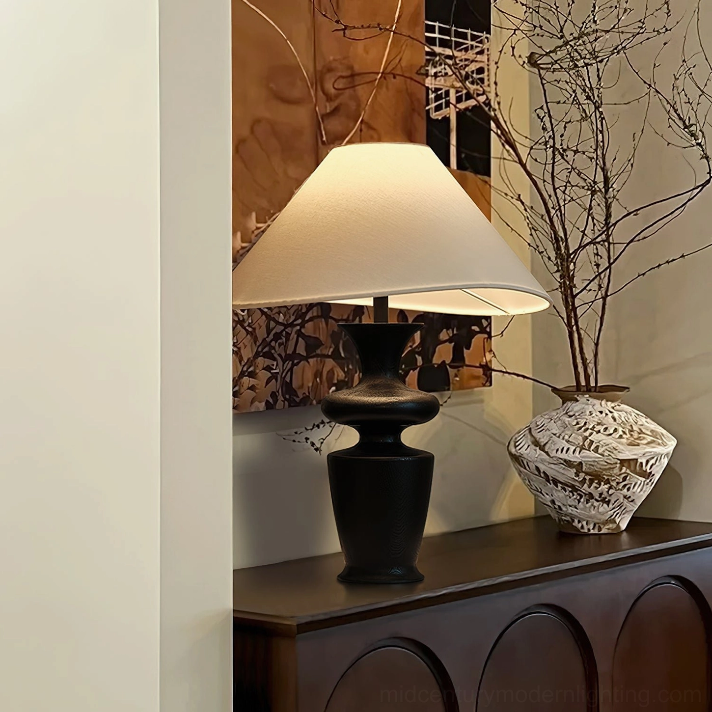 Rhodes lamp with curved wooden base and asymmetrical shade on curved wooden sideboard with floral arrangement