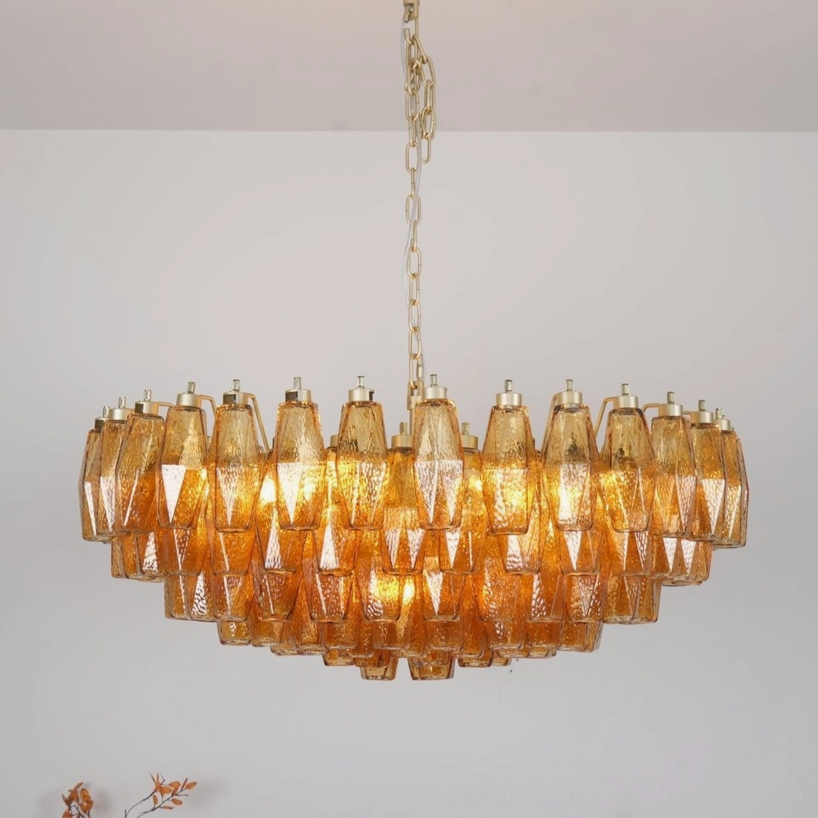 Illuminated rhombus Murano chandelier showing warm amber glass glow with gold suspension chain from below